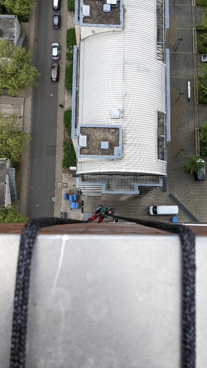 Das Foto zeigt eine spektakuläre Aufnahme über eine Dachabgrenzung auf einem Hochhaus nach unten von einem Profi-Industriekletterer der Firma 'WarDaWas Oberflächen- und Fassadenreinigung für Ihr Gebäude' und dient als Beispiel der Arbeit zu Fassadenreinigung an Hochhäusern und Mehrfamilienhäusern.