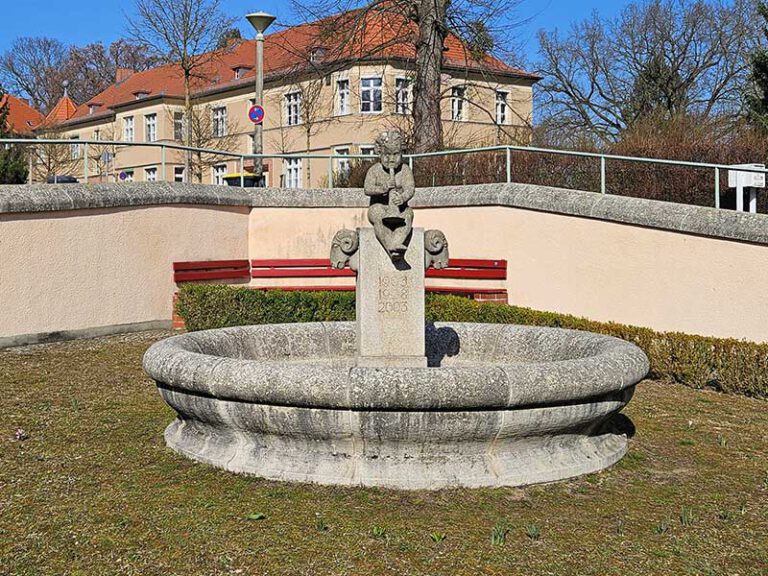 Das Bild zeigt den Brunnen in der Kunersdorfer Straße in Potsdam der nach Jahren der Witterung dunkel verdreckt und mit Flechten bewachsen ist, bevor WARDAWAS ihn gereinigt hat.