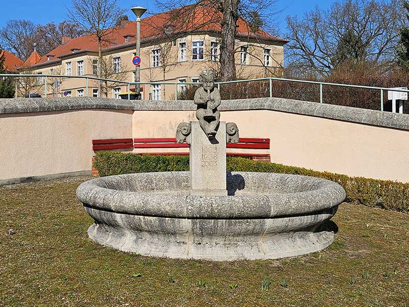 Das Bild zeigt den Brunnen in der Kunersdorfer Straße in Potsdam der nach Jahren der Witterung dunkel verdreckt und mit Flechten bewachsen ist, bevor WARDAWAS ihn gereinigt hat.