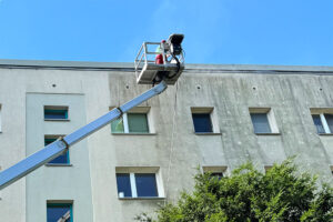 Das Foto zeigt einen Mitarbeiter des WARDAWAS-Teams bei der Fassadenreiningung eines potsdamer Wohnblocks auf der Hebebühne.