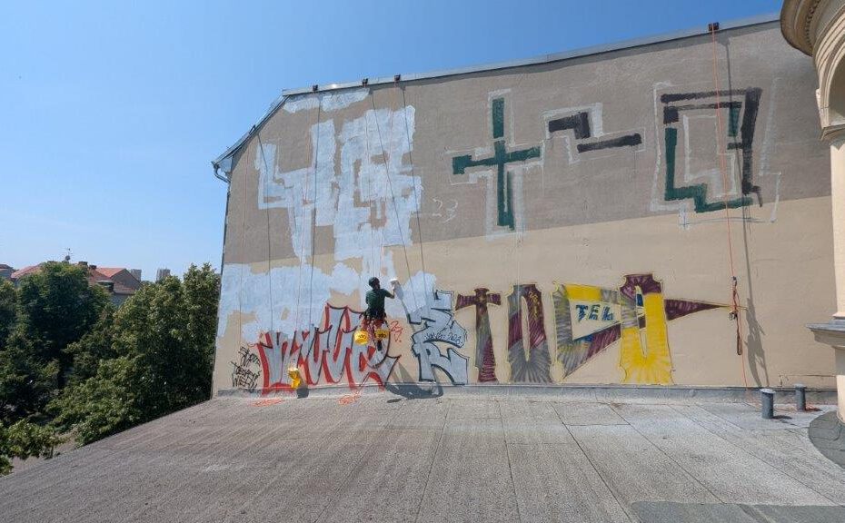 Das Bild zeigt die mit Graffitis beschmierte Fassade der Potsdamer Stadtverwaltung die von WarDaWas professionell von einem Industriekletterer gereinigt wird