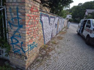 Das Bild zeigt eine Klinkermauer in Potsdam die mit Grafitti-Schmierereien übersäht ist und anschließend von WarDaWas GmbH professionell gereinigt wird