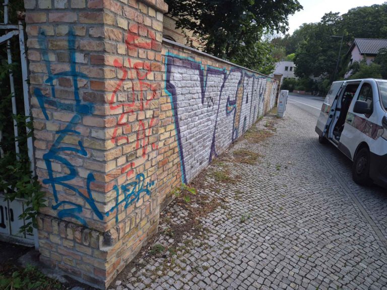 Das Bild zeigt eine Klinkermauer in Potsdam die mit Grafitti-Schmierereien übersäht ist und anschließend von WarDaWas GmbH professionell gereinigt wird