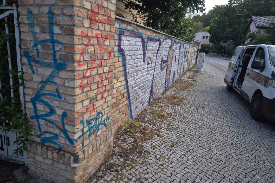 Das Bild zeigt eine Klinkermauer in Potsdam die mit Grafitti-Schmierereien übersäht ist und anschließend von WarDaWas GmbH professionell gereinigt wird