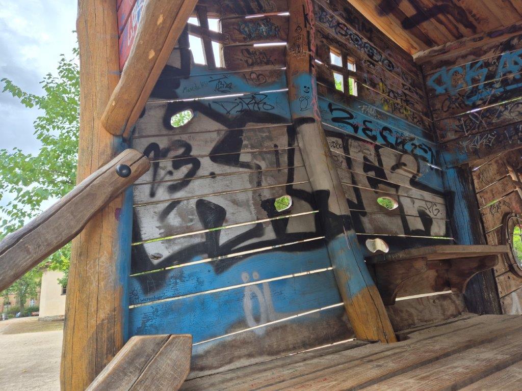 Das Bild zeigt mit Graffitis beschmierte Innenwände eines auf Stelzen stehenden Kletterhäuschen auf einem Spielplatz in Potsdam Babelsberg, bevor es professionell und umweltfreundlich von der Firma WarDaWas gereinigt wird.