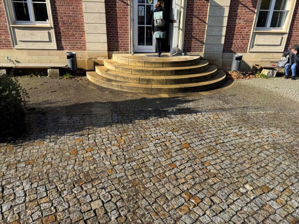 Das Bild zeigt den Eingangsbereich der Univeristät Postdam, dessen Pflastersteine auf dem Boden von Graffitis gereinigt wurden und bebildert den Beitrag 'Von Tags bis Taubenkot: Ein Jahrzehnt Reinigungseinsätze für die Universität Potsdam' der Firma WarDaWas.