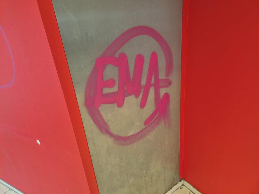 Das Bild zeigt eine Metallfläche im Innenraum einer Sparkasse, das mit Graffiti beschmiert ist.