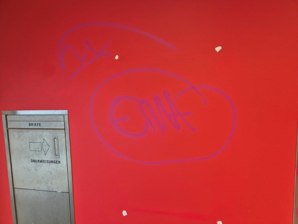 Eine rote Wand im Innenraum einer Sparkasse, die mit Graffiti beschmiert wurde.